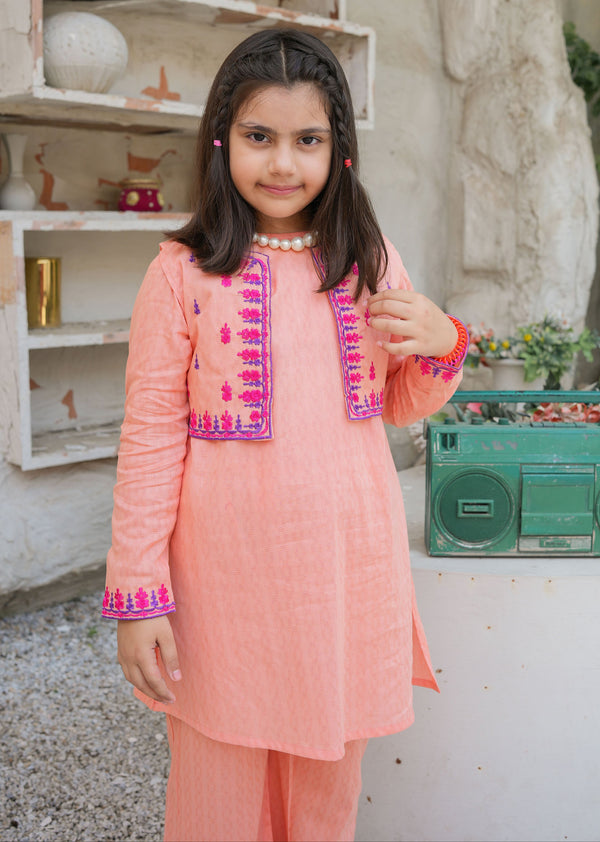 Young girl in a peach traditional outfit standing in front of a rustic shelf and green radio.